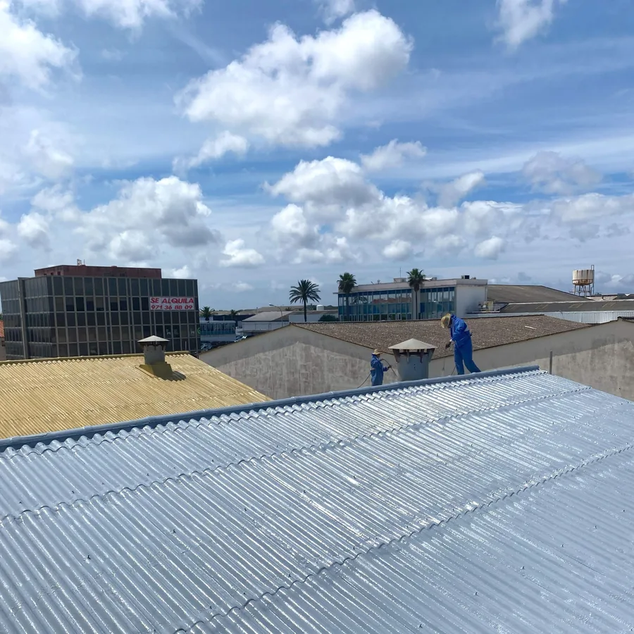 Workers in blue suits spraying a silver polyurea membrane on a corrugated industrial roof for asbestos encapsulation