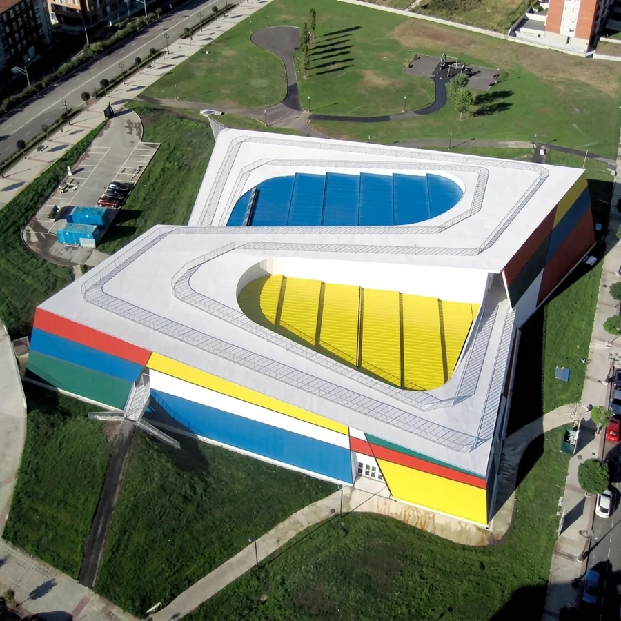 Aerial of a geometric building with a white Impermax ST roof, blue and yellow recessed tiers, red yellow blue facade panels