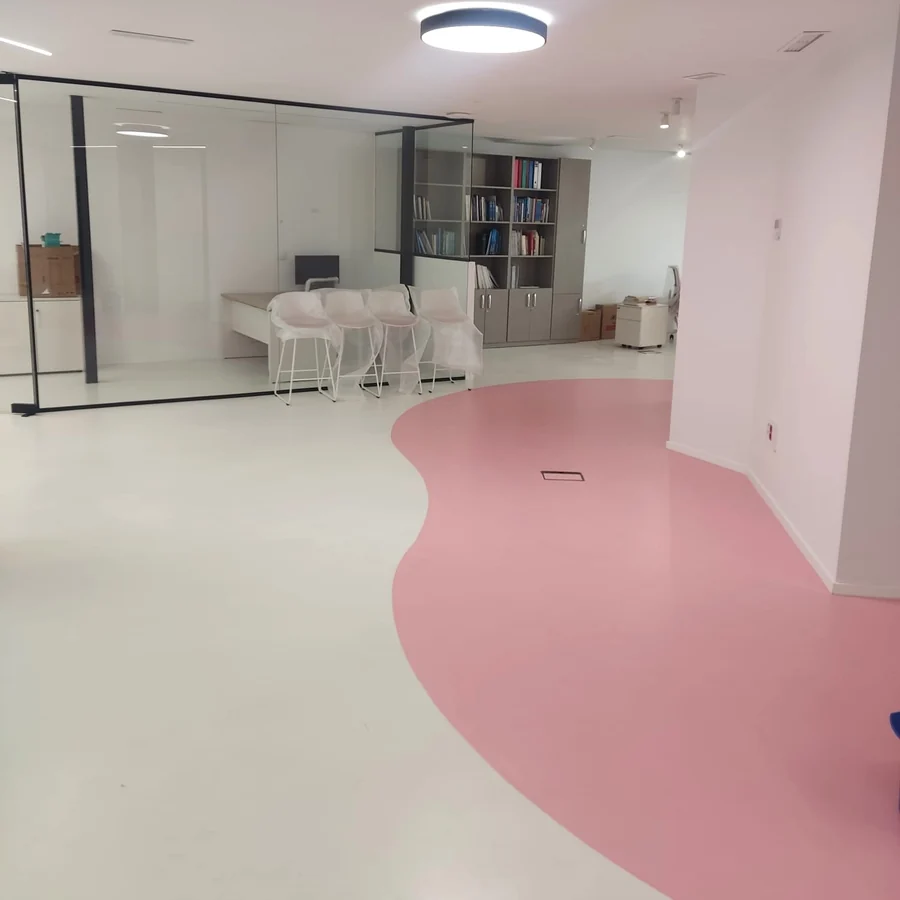 Seamless white and pink curved resin floor in a dental clinic interior, glass office partition and plastic-covered chairs