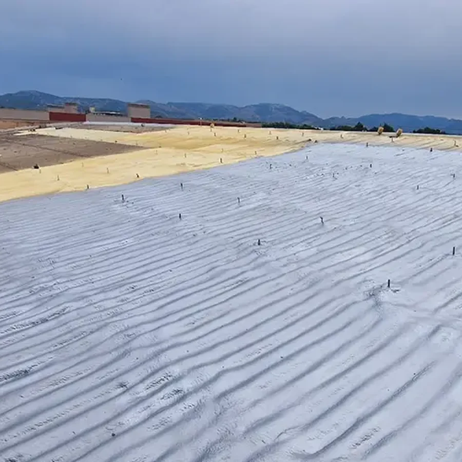 Roof encapsulation in progress: yellow spray foam with depth pins beside a light-grey polyurea membrane, mountains on the horizon
