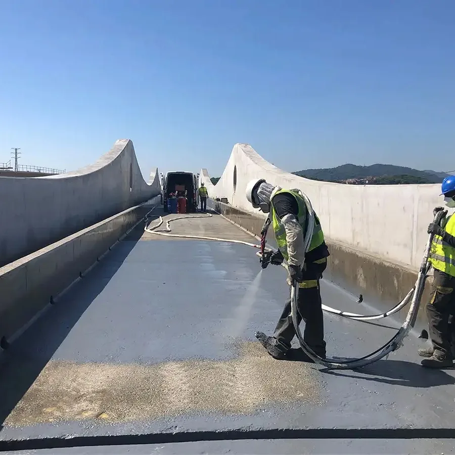 Applicators hot-spraying a grey-blue polyurea membrane on a concrete bridge deck with curved parapet walls