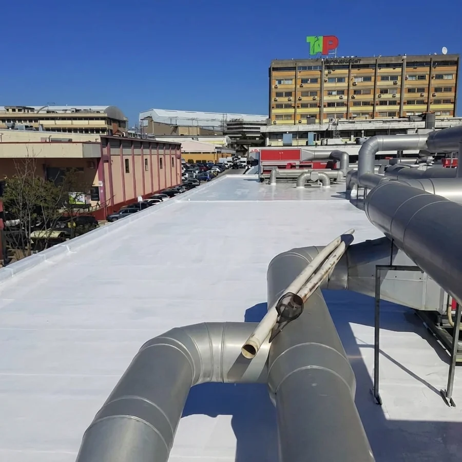 White solar-reflective aliphatic roof membrane on an industrial deck, HVAC ducts in the foreground, clear sky