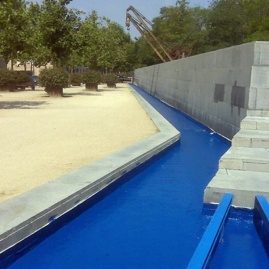 Outdoor royal-blue Impermax Aqua 2K channel beside a grey stone wall, gravel walk and trees