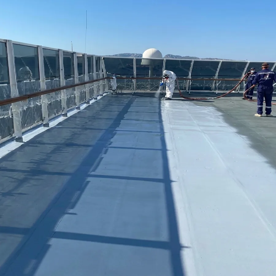 Worker in a white suit spraying a light-blue marine-deck coating, hose crew behind, glass railing masked in plastic