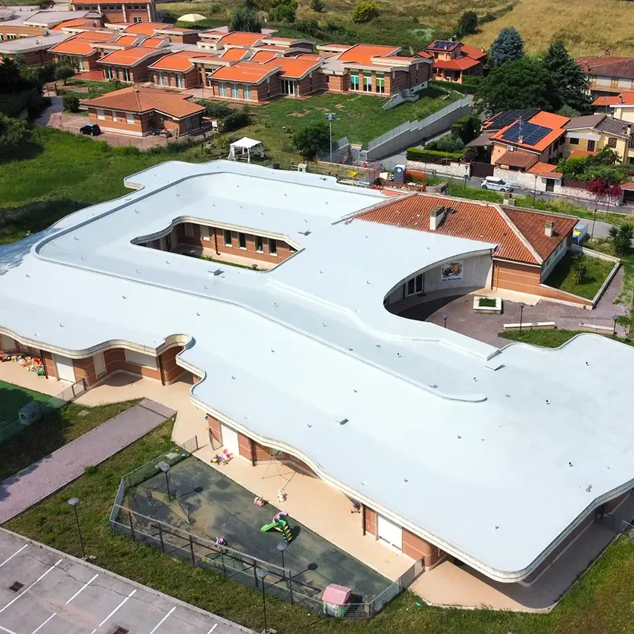 Aerial of a nursery-school building with a seamless light-grey-white flat roof, courtyard cut-out, brick walls and playground