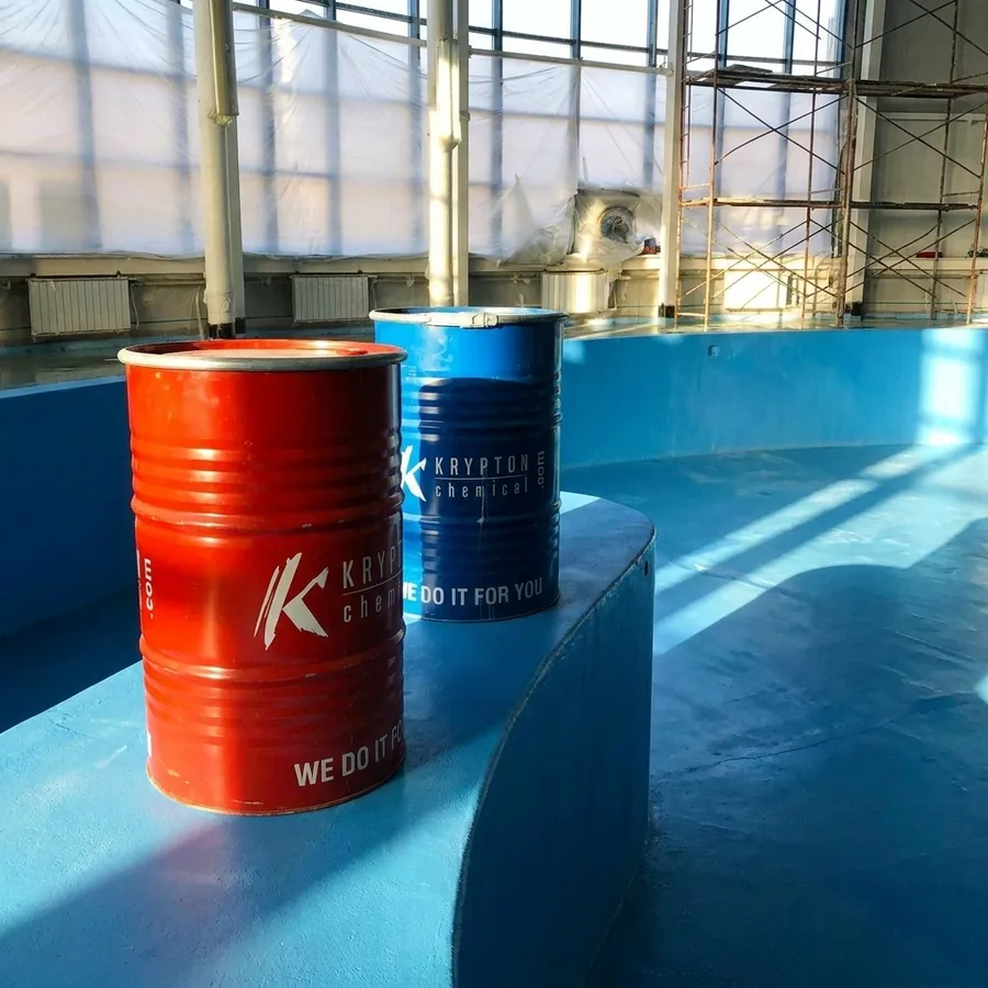 Red and blue Krypton Chemical drums on a blue-coated circular tank interior with sunlight through large windows