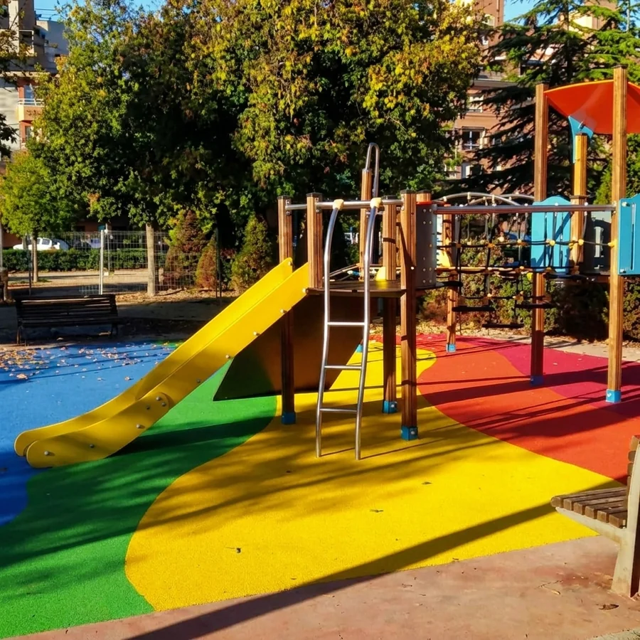 Children’s playground in Granada with a yellow slide on poured-in-place rubber safety flooring in blue, green, yellow and red