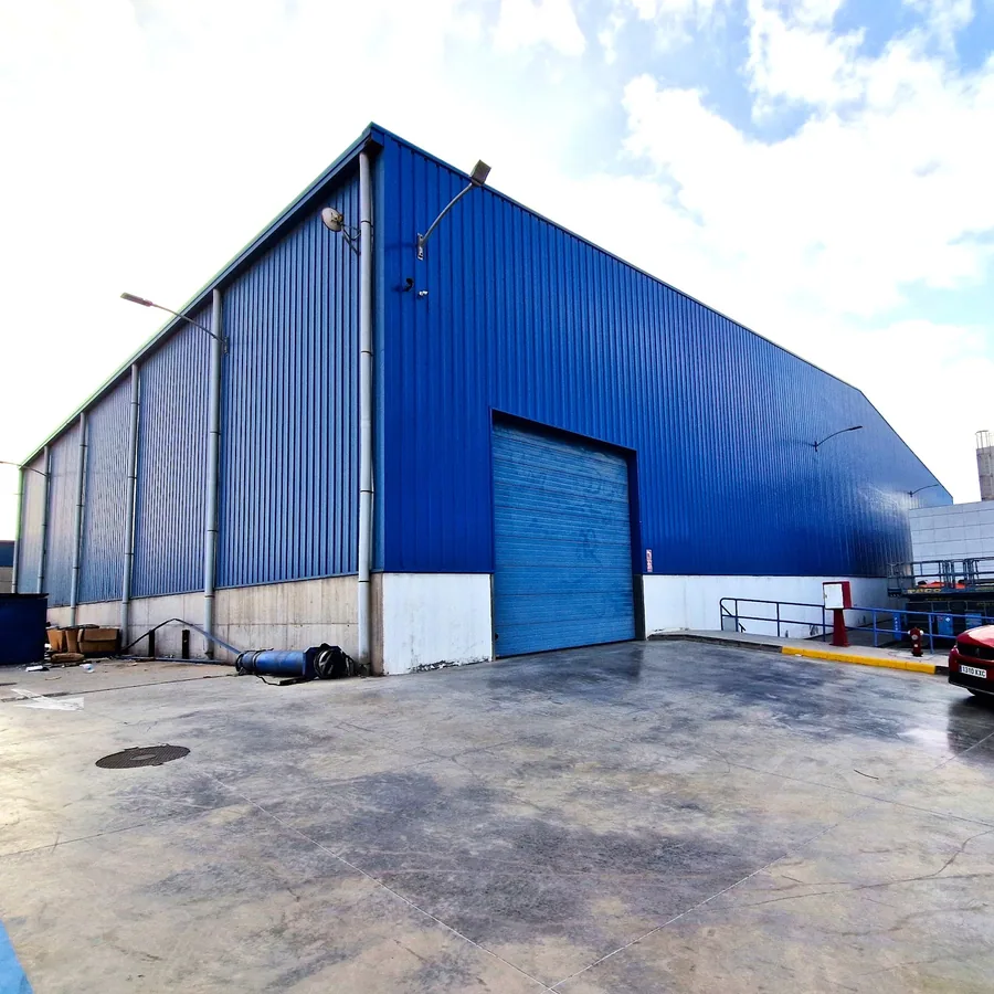 Blue corrugated industrial warehouse with a large roll-up door and concrete yard specified with ProLine AB95P