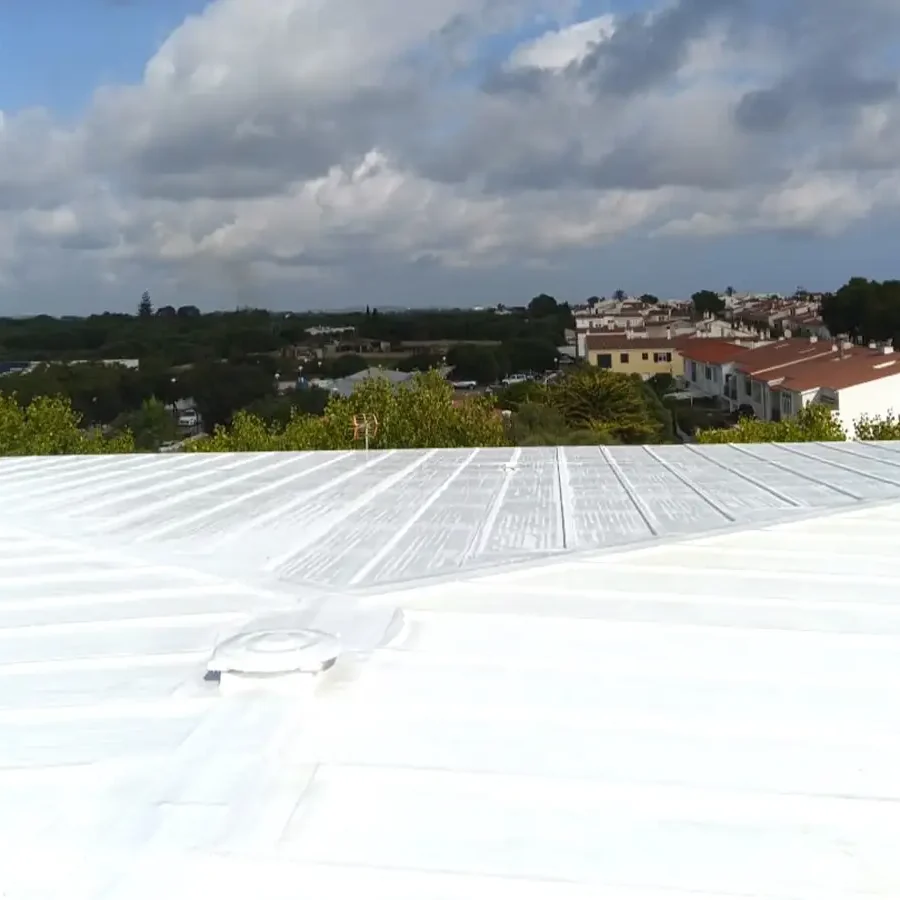 Bright white cool-roof membrane on a sports-pavilion deck with a coated circular vent, trees and tiled houses beyond