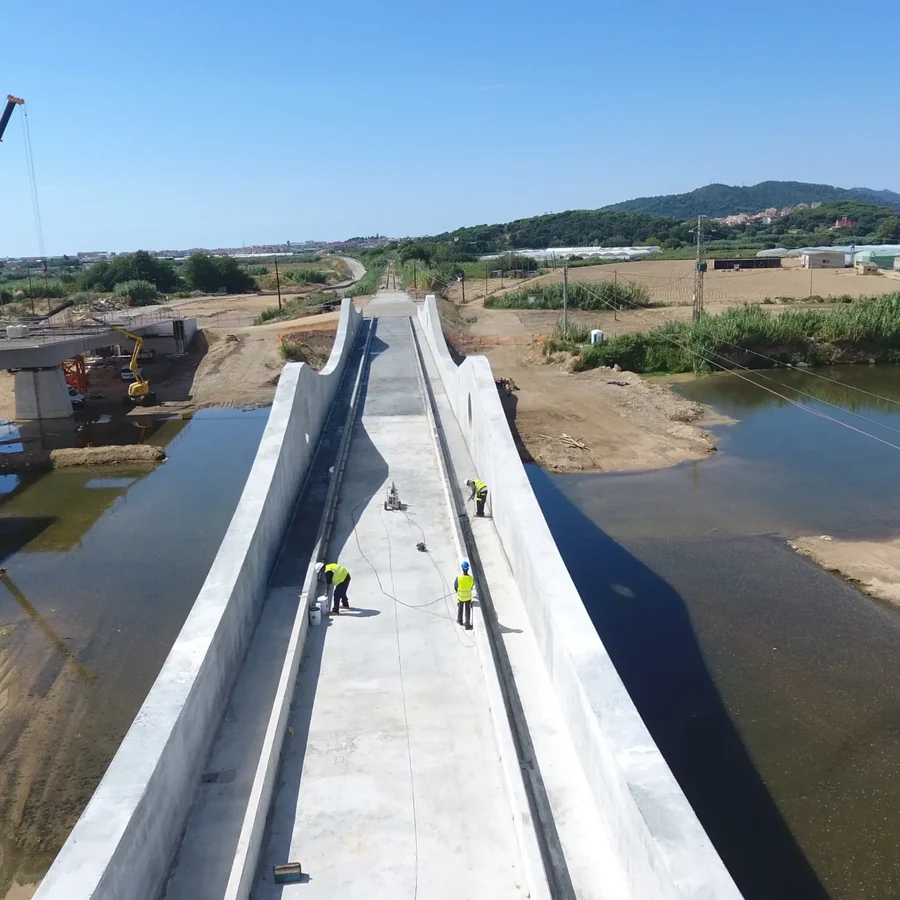 Aerial of the Tordera railway bridge deck with workers in yellow vests, hoses and a bucket on the concrete, river below