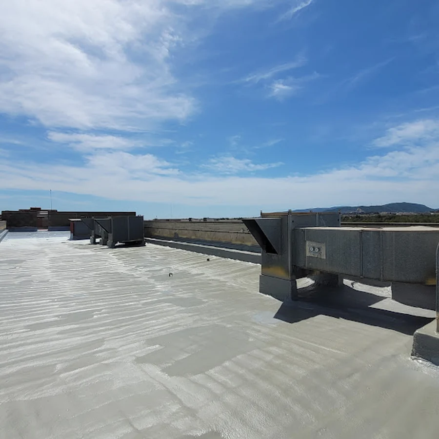 Light-grey liquid membrane on a flat UIB roof with metal HVAC units, parapet and hills under a clear sky