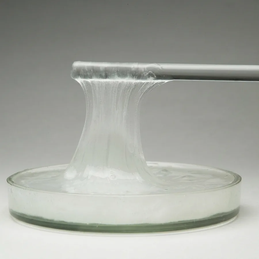 White viscous liquid membrane stretching in a cohesive column from a glass dish to a metal rod