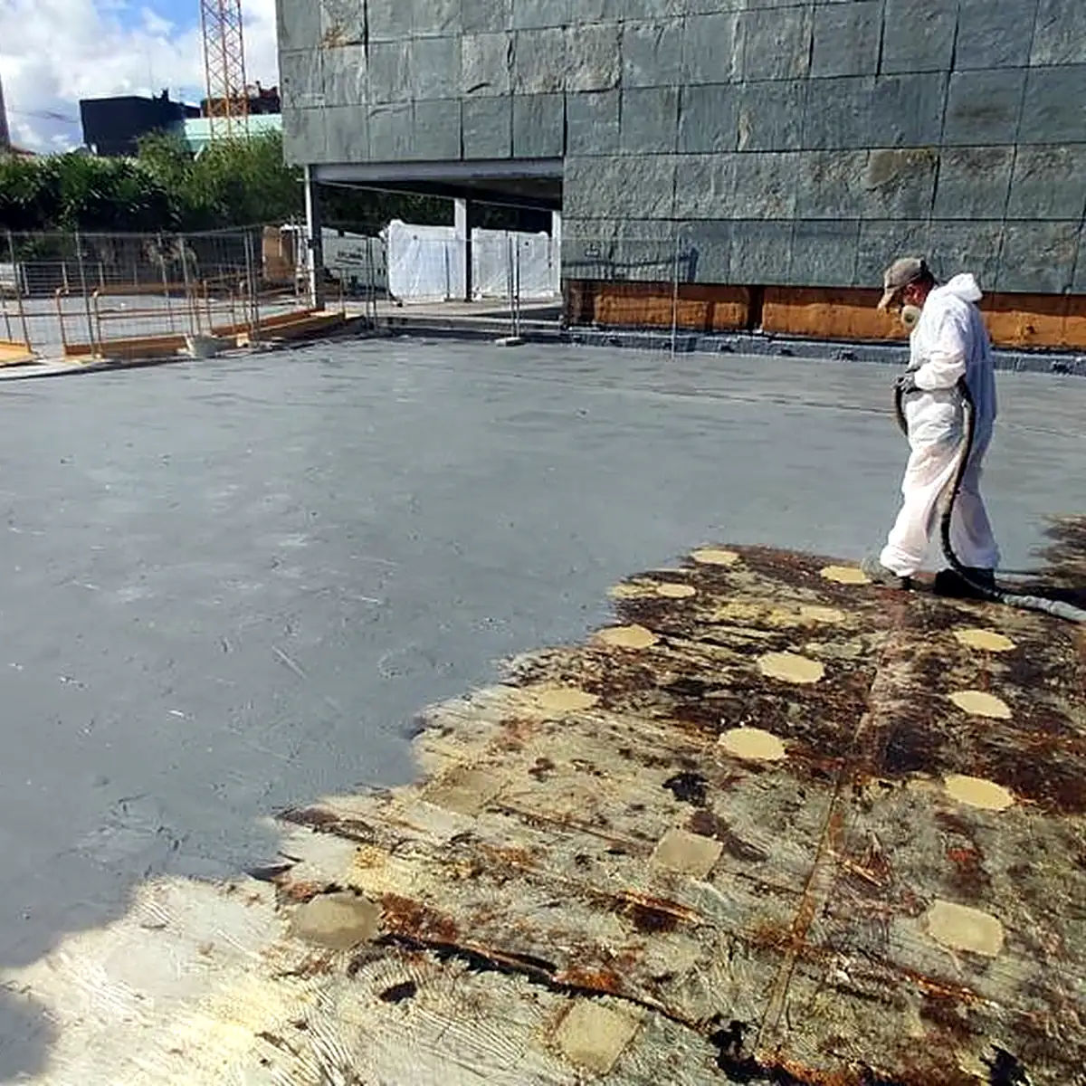 Worker in a white suit spraying the grey membrane on the terrace Worker in a white suit spraying the grey membrane on the terrace