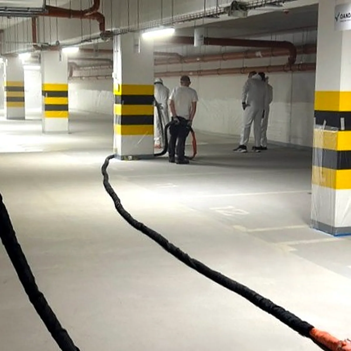 Spray hose running across the grey deck between yellow-striped pillars, Kraków car park