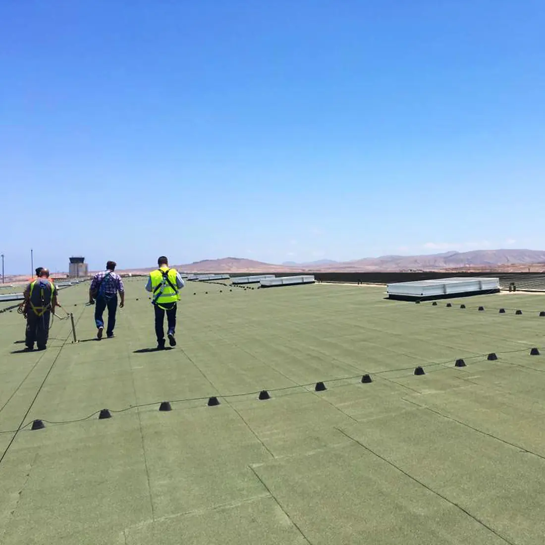 Three workers walking the green membrane, with the control tower behind