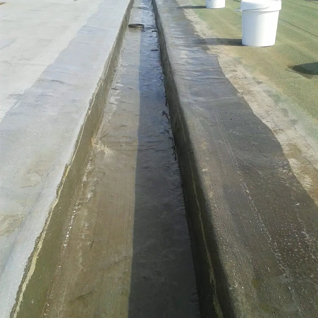 Long gutter between the coated area and the green membrane, with buckets along it