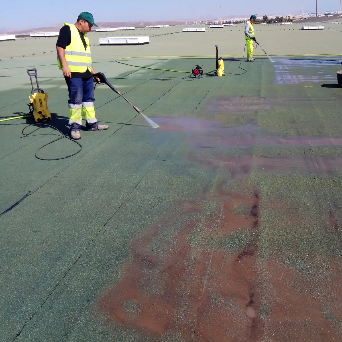 Workers pressure-washing the green membrane on the airport roof