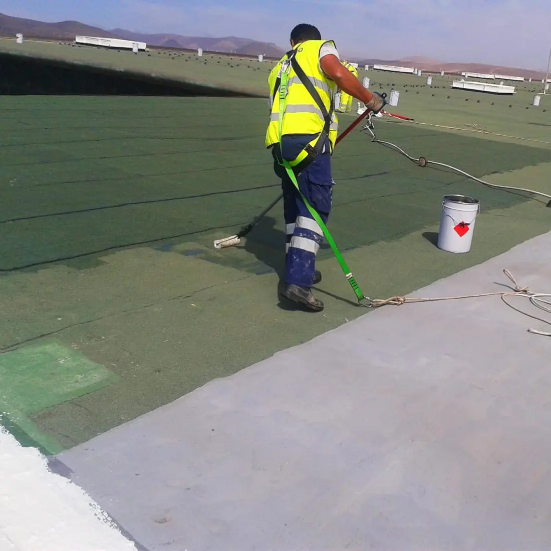 Worker rolling the edge where the grey coat meets the green membrane