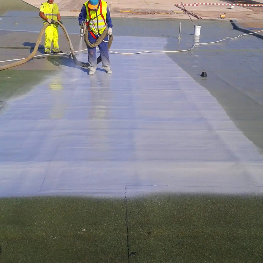 Worker spraying the light grey coat onto the green airport roof
