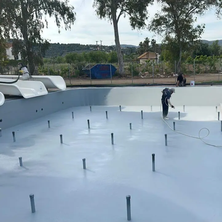 Worker spraying the light coat in an empty basin, with floor pipes in place Worker spraying the light coat in an empty basin, with floor pipes in place