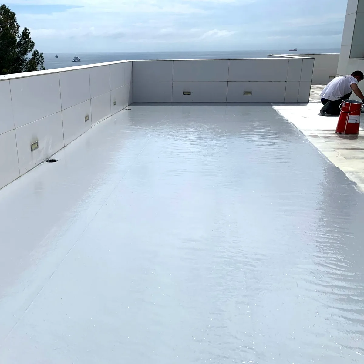 Freshly coated light grey roof with the sea behind and an applicator at the far end, Platja Arrabassada, Tarragona