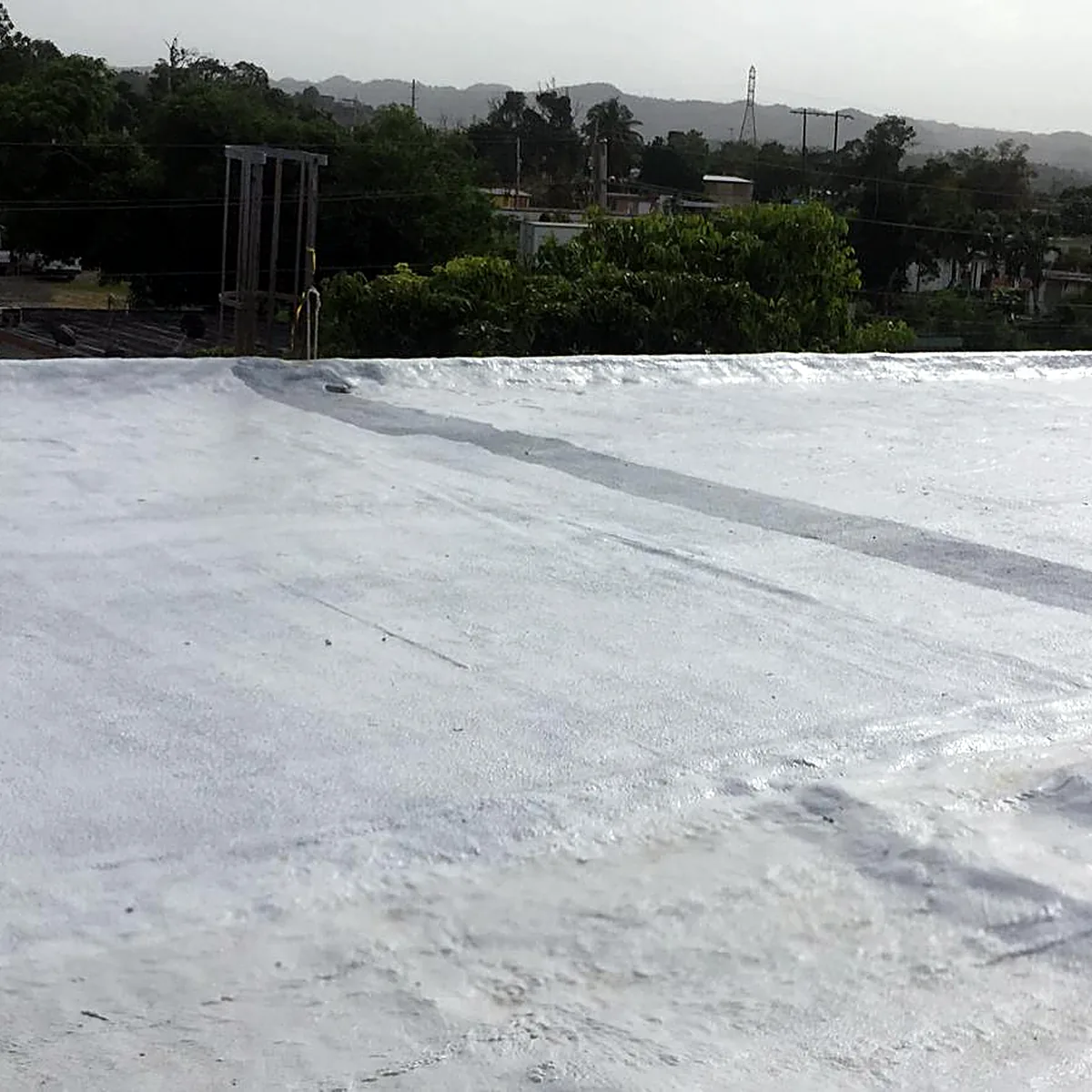 White roof running to its edge, with trees, houses and hills beyond White roof running to its edge, with trees, houses and hills beyond