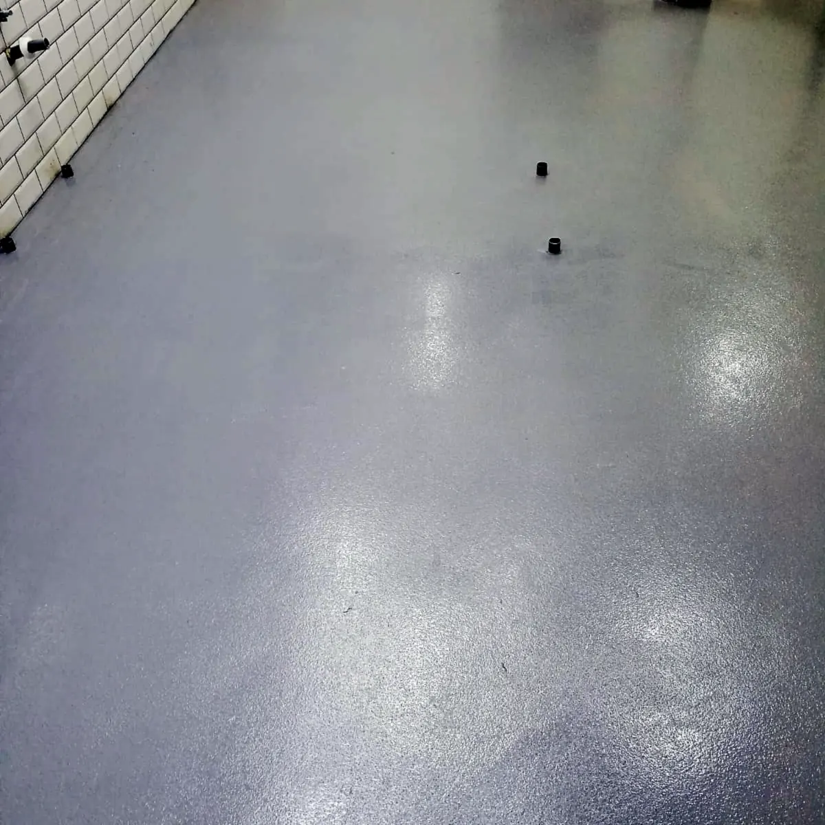 Empty kitchen aisle with the grey epoxy floor along a white tiled wall