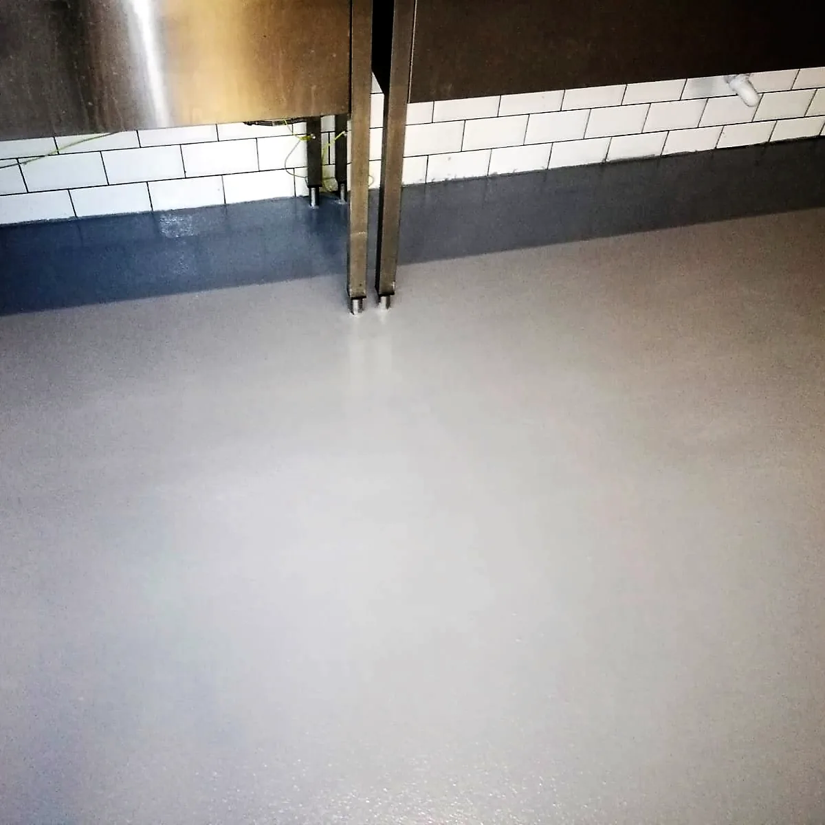 Grey epoxy floor running under stainless counters against a tiled wall