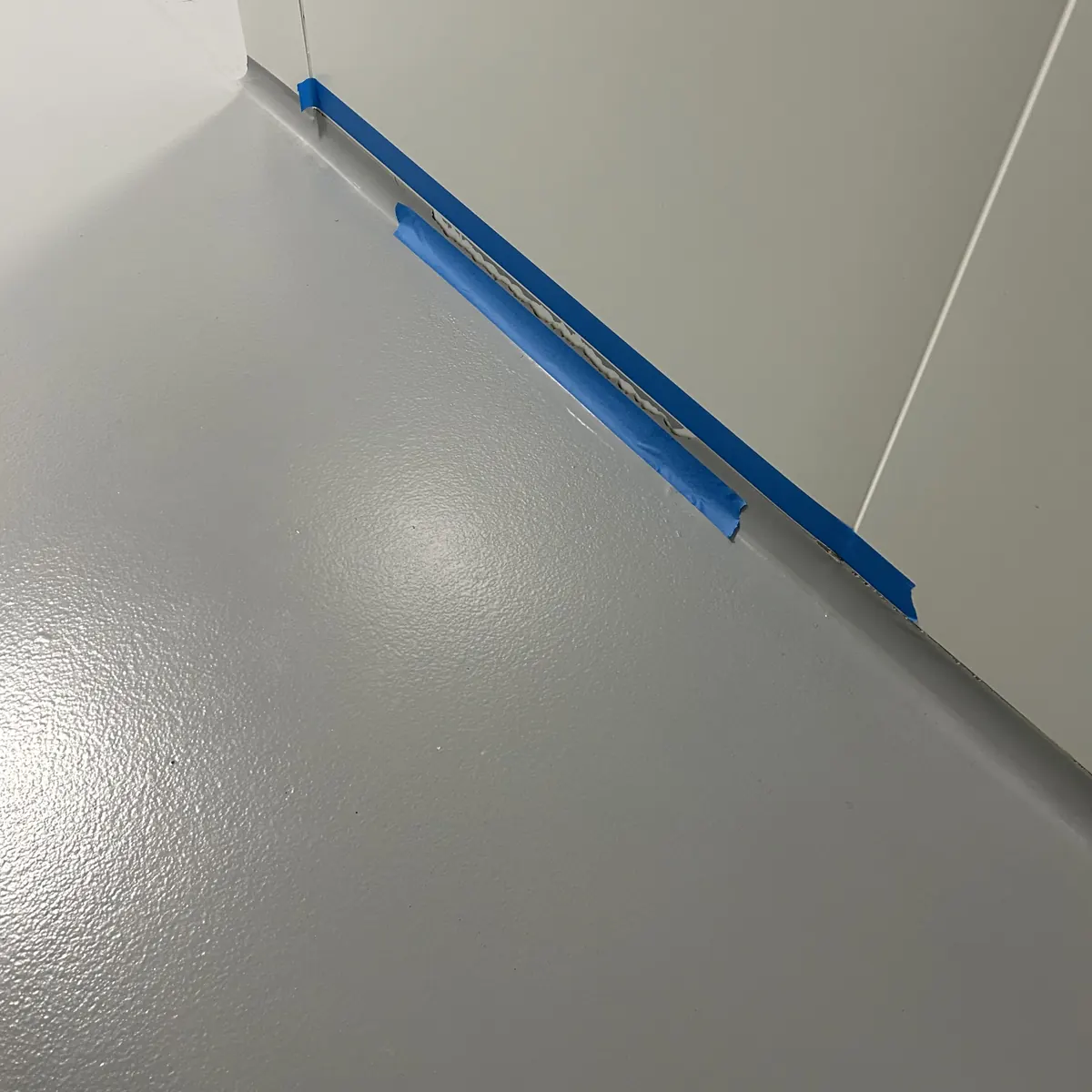 Encuentro entre suelo y pared con cinta azul durante la aplicación del epoxi, Aiguaviva