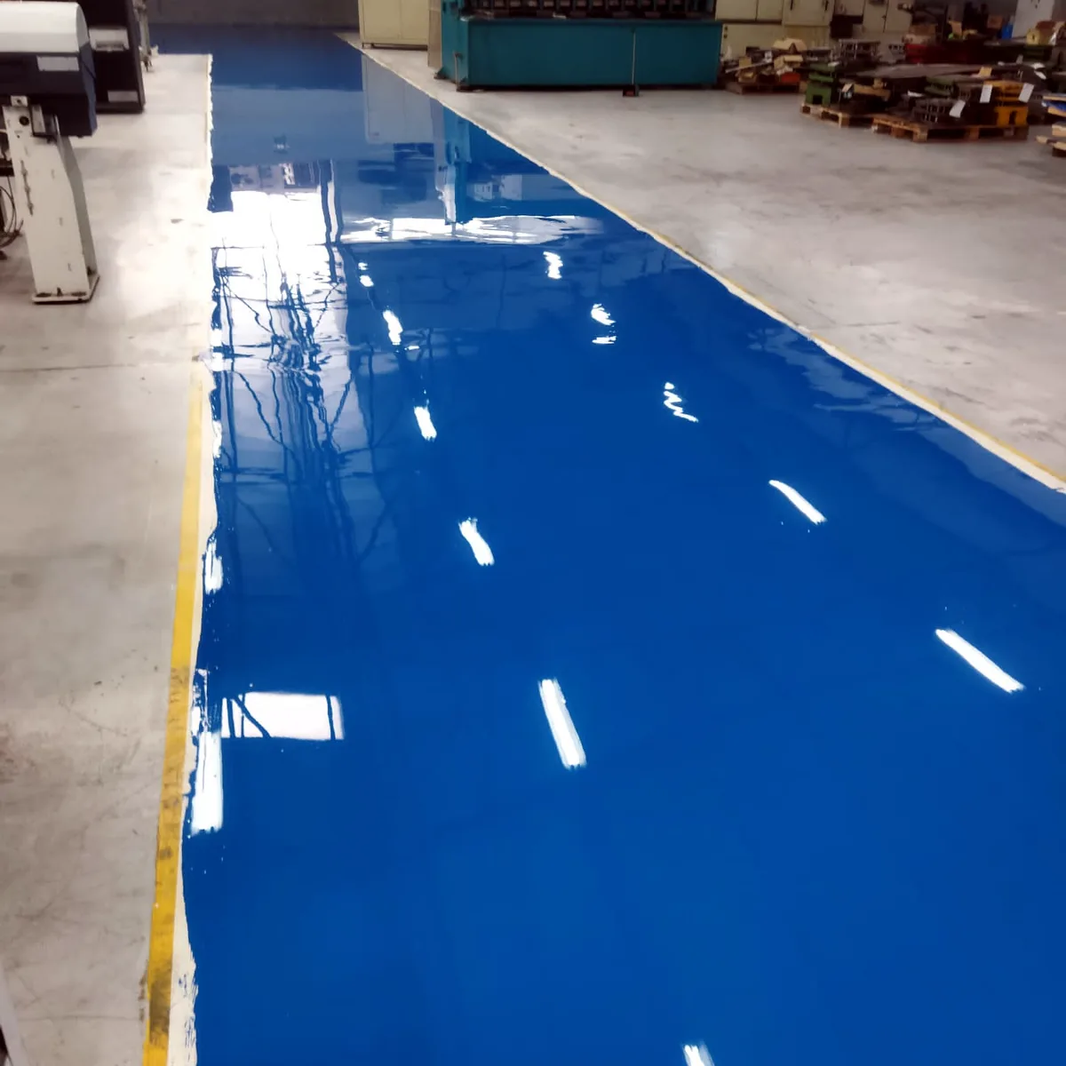 Glossy blue walkway past machines with a yellow edge line, Porto