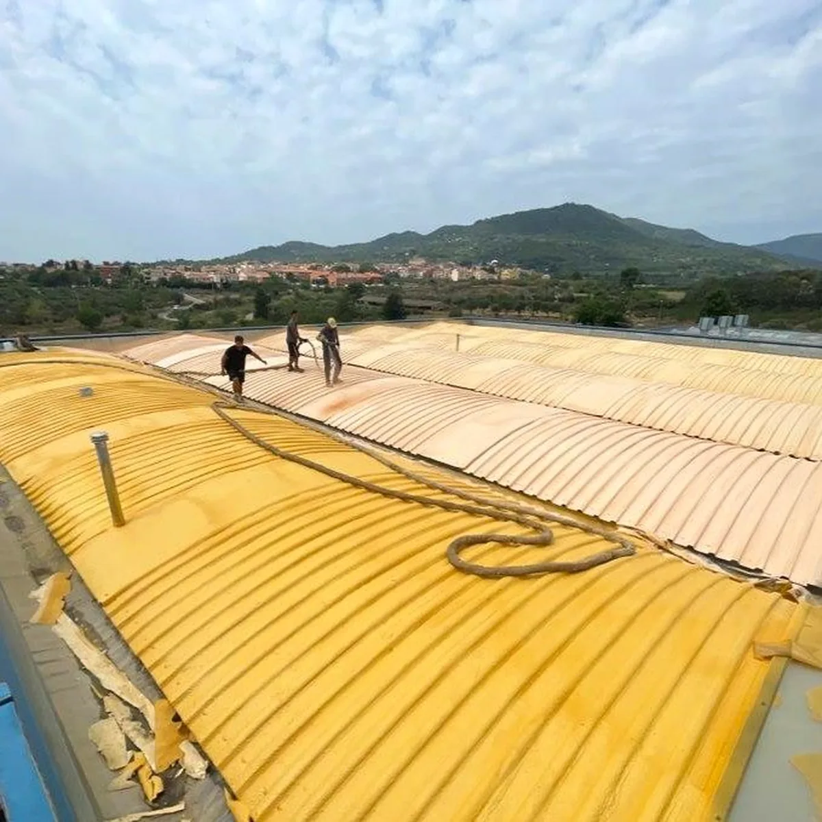 Wide view of the foamed warehouse roof with hills behind, La Selva del Camp