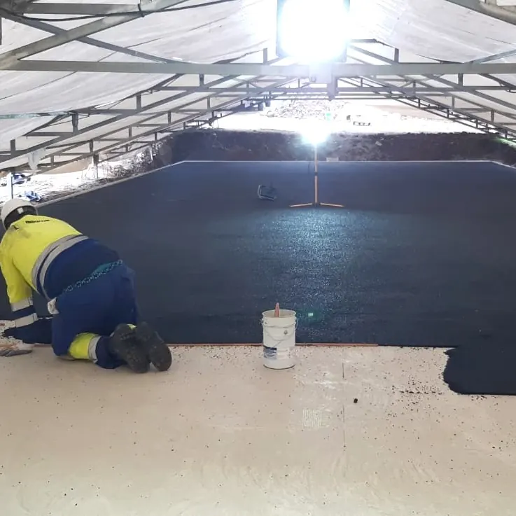 Worker kneeling to finish the edge of the black layer