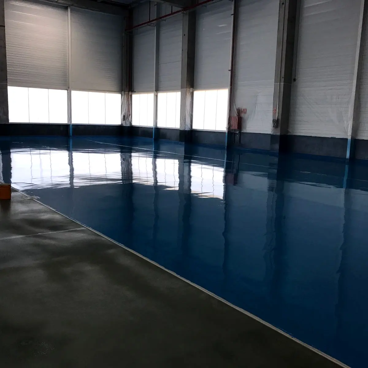 Blue resin floor meeting uncoated concrete in the hall, Algeria pharma plant