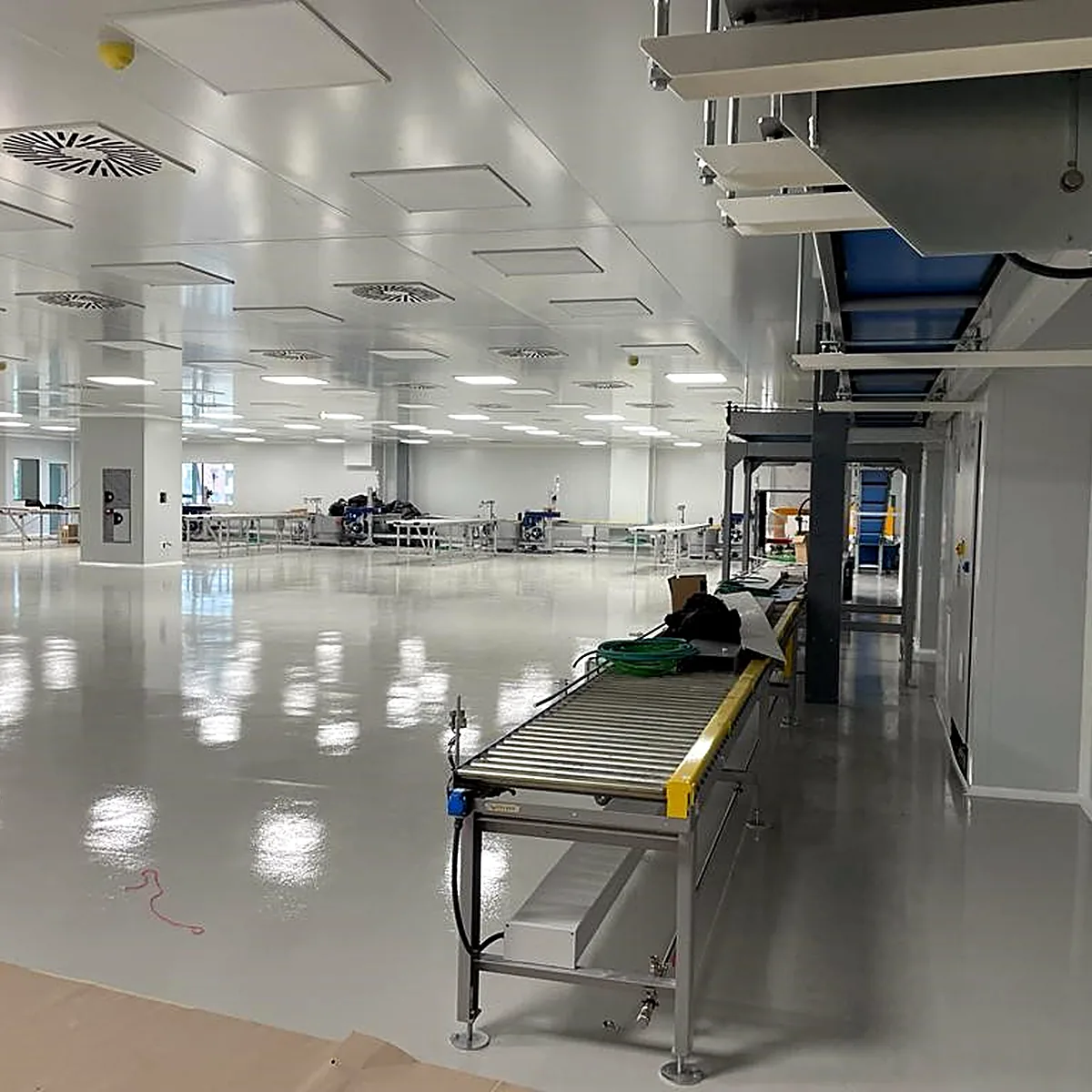 Light grey floor beside a roller conveyor and white wall panels