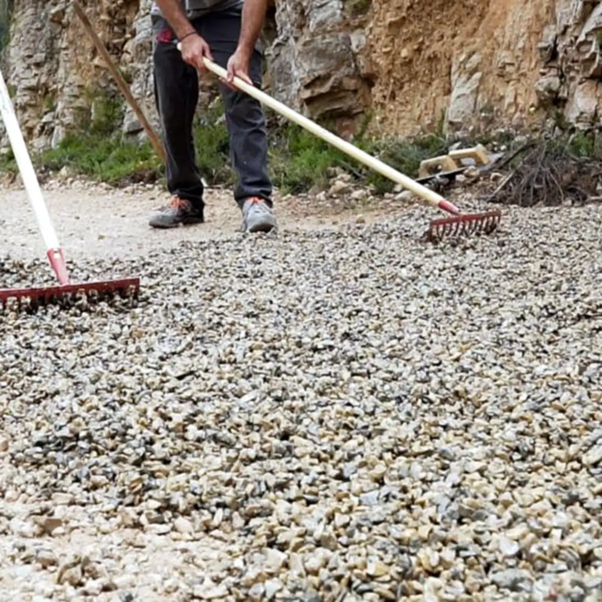 Two workers levelling the stone mix with rakes beside a rock face Two workers levelling the stone mix with rakes beside a rock face