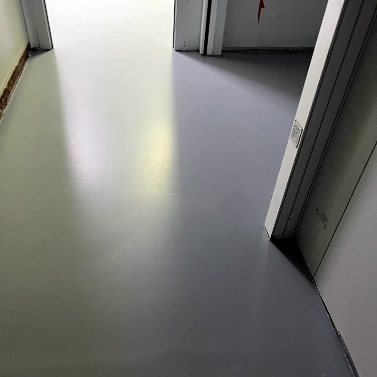 Finished light grey floor in a corridor between white doors
