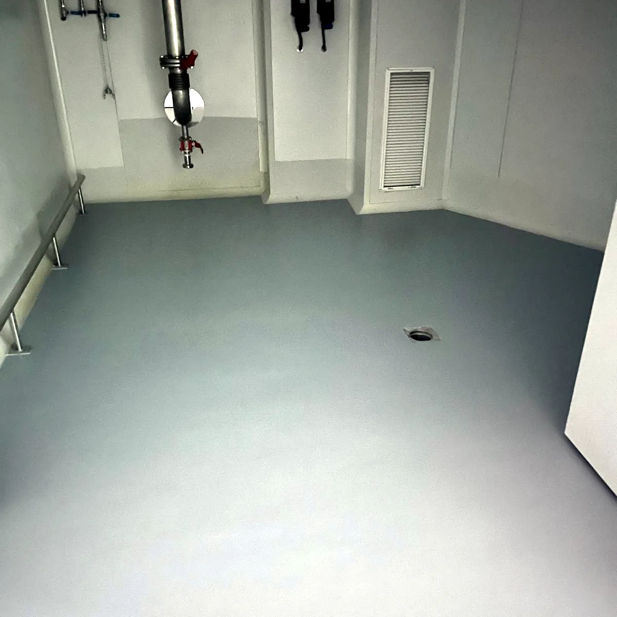 Grey floor in a room with pipework and a wall hatch