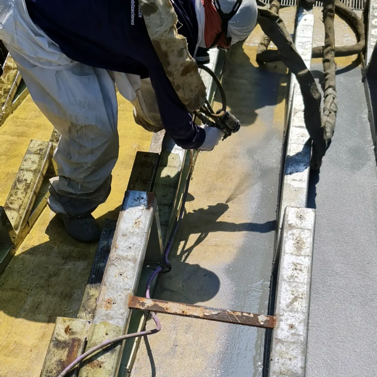 Close-up of the spray gun coating a roof channel beside a steel frame