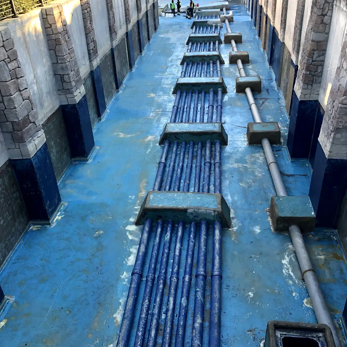 Blue-lined channel with pipe manifolds and stone-clad walls, Parque Warner Madrid