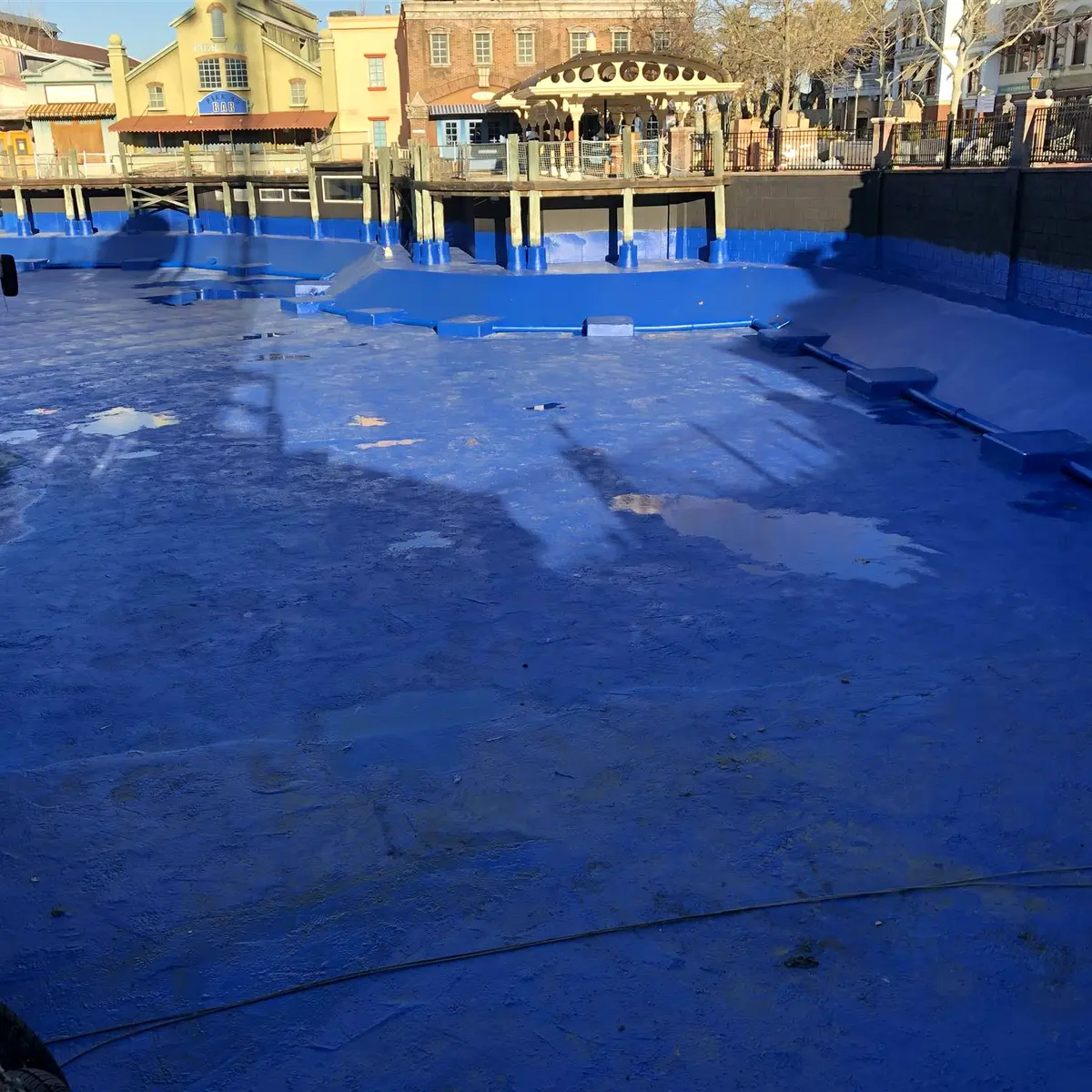 Large basin floor lined in blue below themed buildings, Parque Warner Madrid