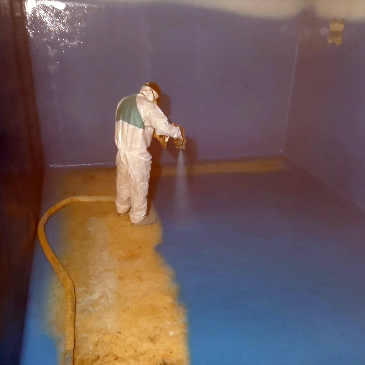 Applicator spraying the blue water tank lining on the floor, Palma