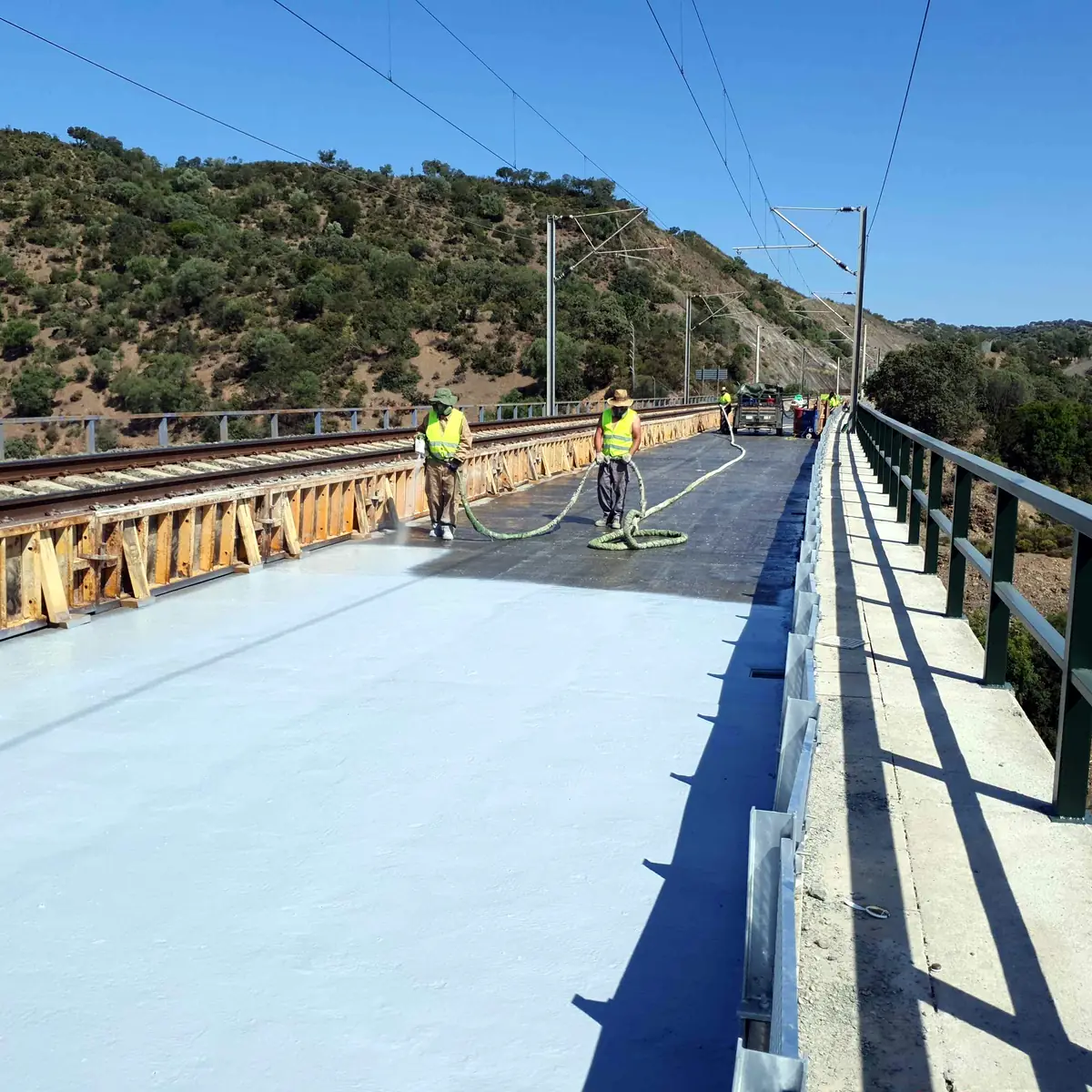 Two workers on the deck beside the steel girders, with hills behind Two workers on the deck beside the steel girders, with hills behind