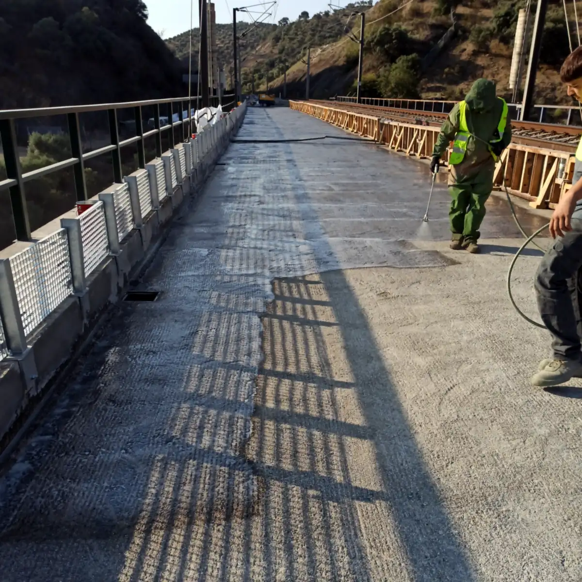 Worker in a protective suit spraying the grey coat by the rail girders Worker in a protective suit spraying the grey coat by the rail girders