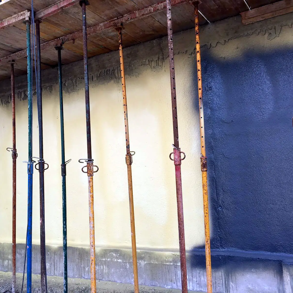 Yellow foam primer and grey membrane meeting behind the props of the slab above