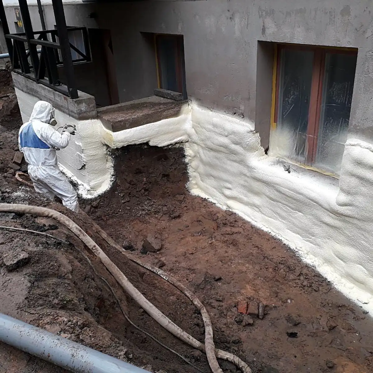 Applicator spraying Rayston Spray Primer 150 foam on a foundation wall beside the excavation