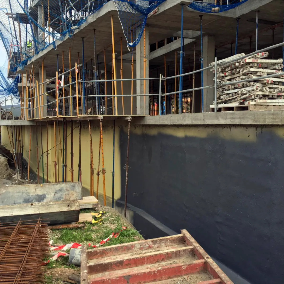 Long foundation wall with the grey membrane under scaffolding, residential site