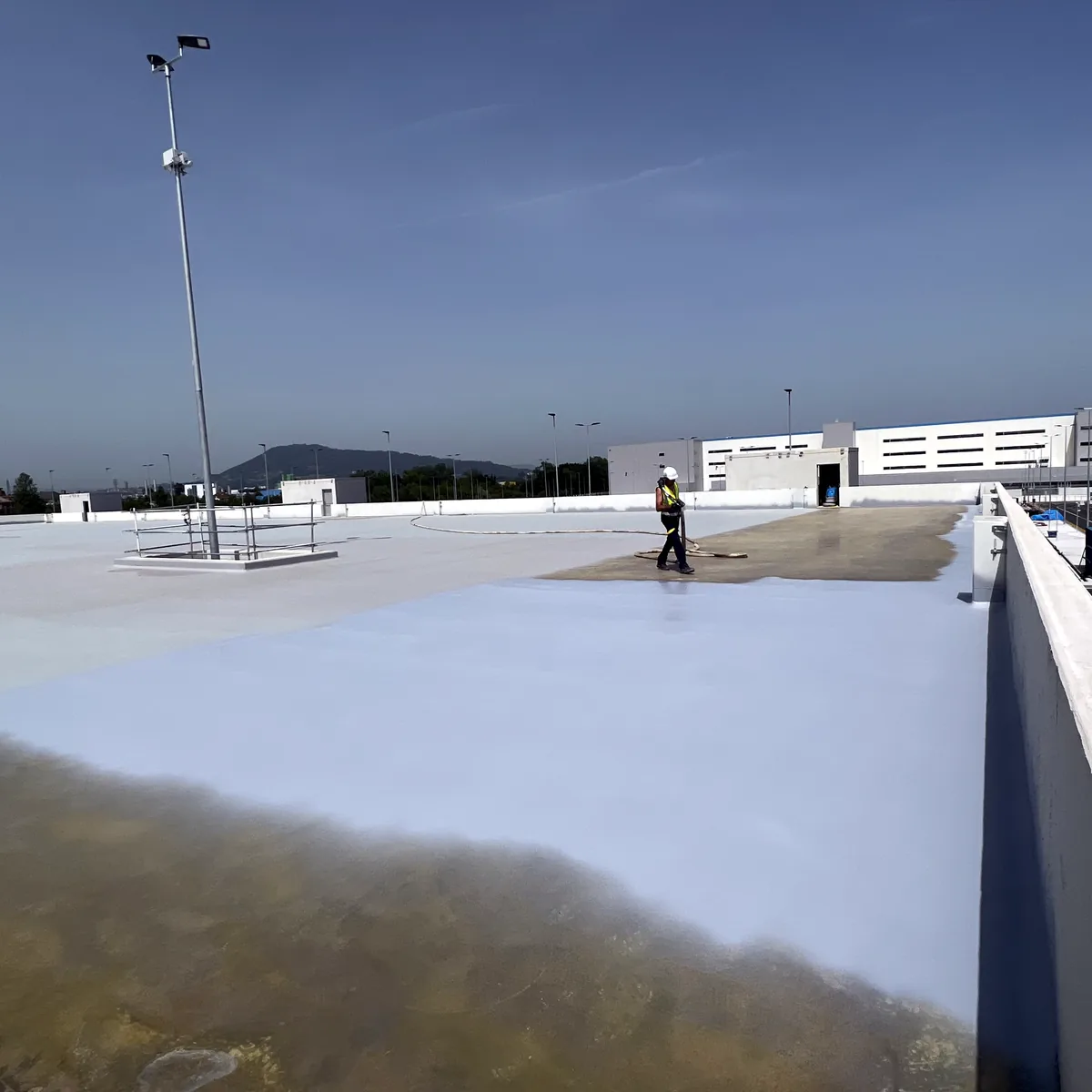 Worker far along the rooftop parking waterproofing in La Línea, near the parapet
