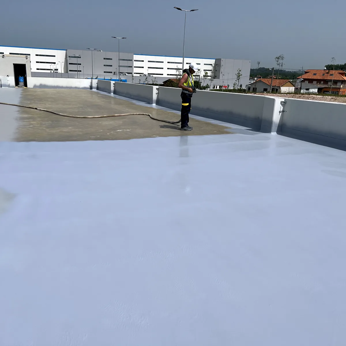 Rooftop parking waterproofing in La Línea: applicator spraying along the parapet