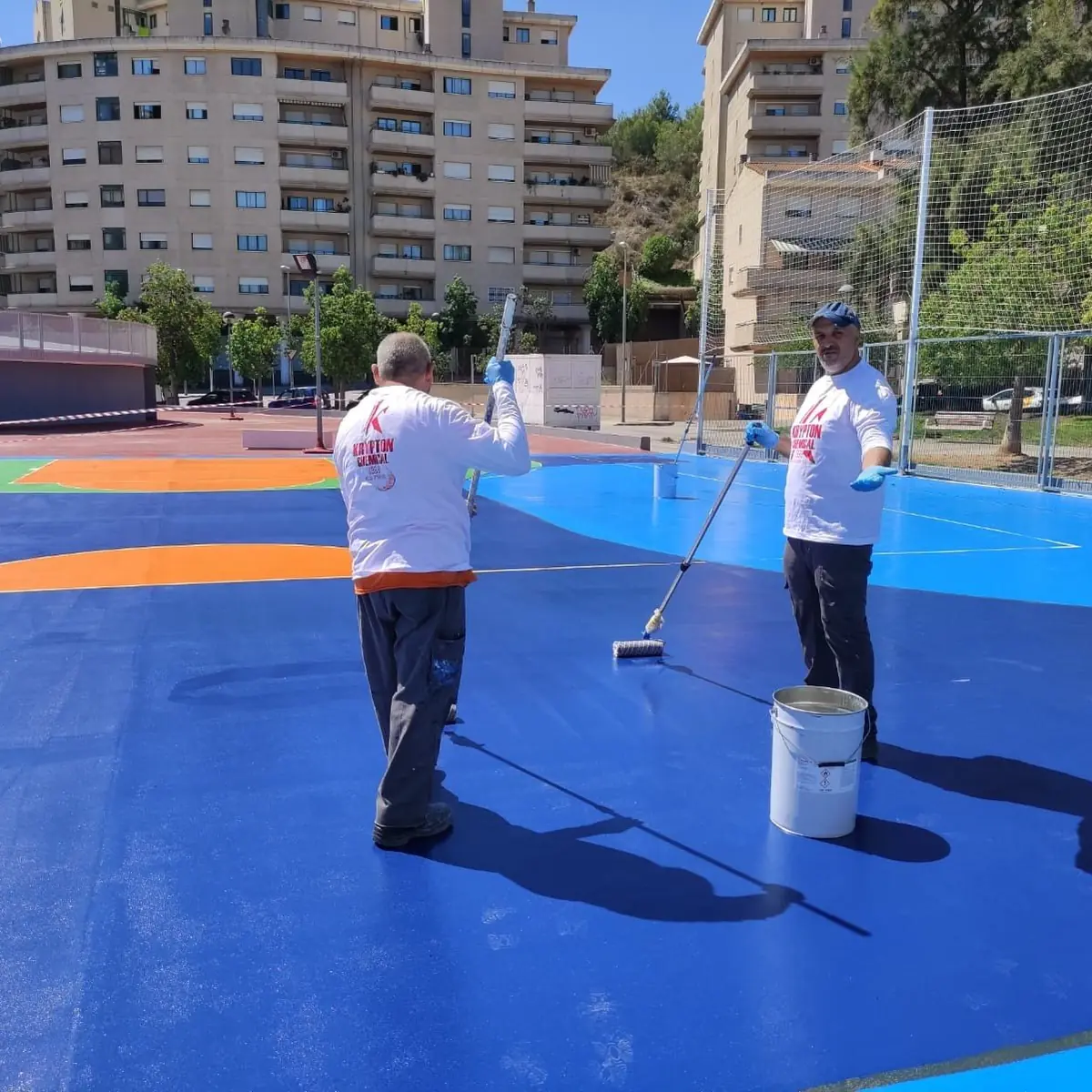 Crew applying blue polyurethane coat with pails on the rooftop court, Barcelona