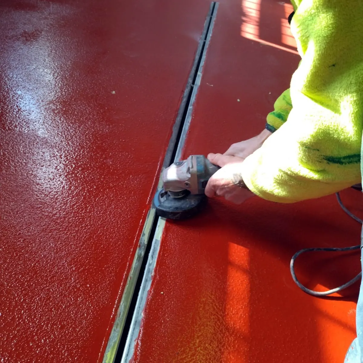 Worker using an angle grinder beside a drain channel in the red floor Worker using an angle grinder beside a drain channel in the red floor